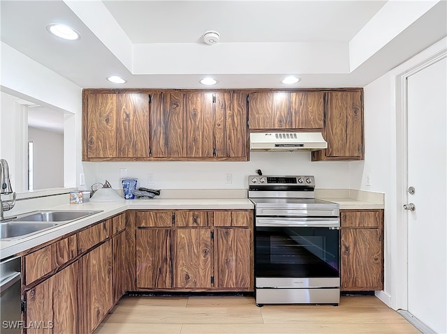 kitchen featuring light wood-type flooring, stainless steel electric stove, a tray ceiling, dishwasher, and sink