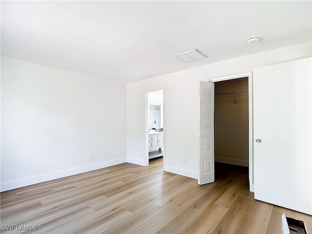 unfurnished bedroom featuring light wood-type flooring, a spacious closet, connected bathroom, and a closet