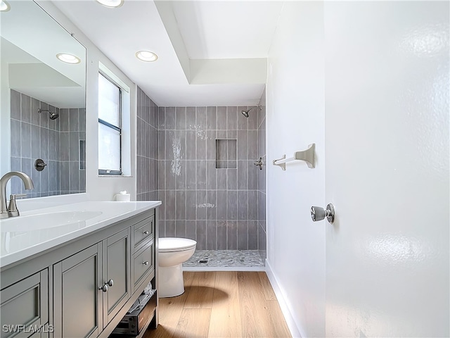 bathroom featuring a tile shower, vanity, hardwood / wood-style floors, and toilet