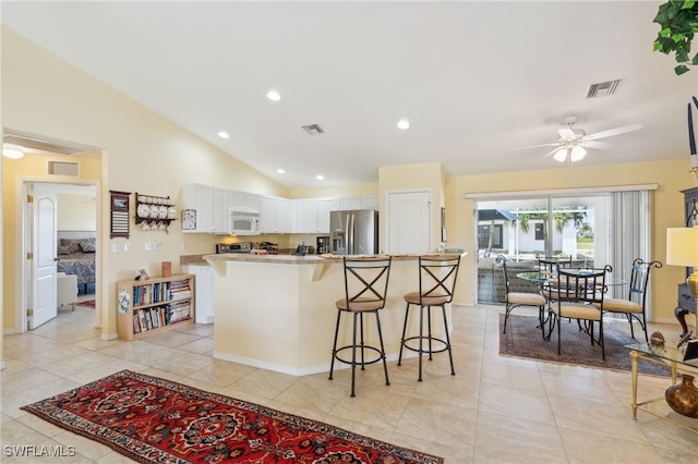 kitchen featuring white cabinetry, vaulted ceiling, a kitchen bar, ceiling fan, and stainless steel fridge