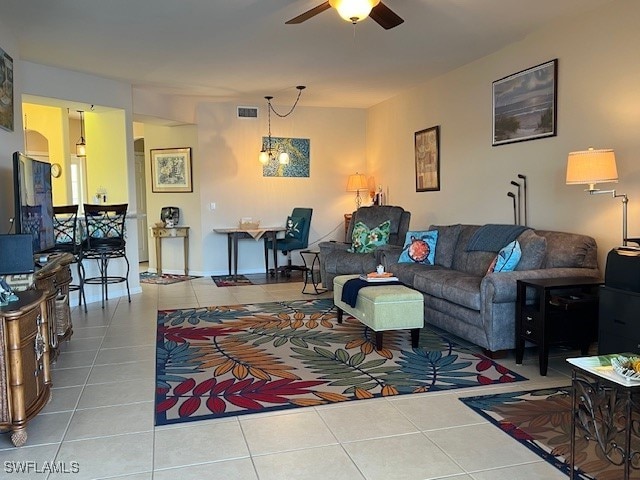 tiled living room with ceiling fan with notable chandelier