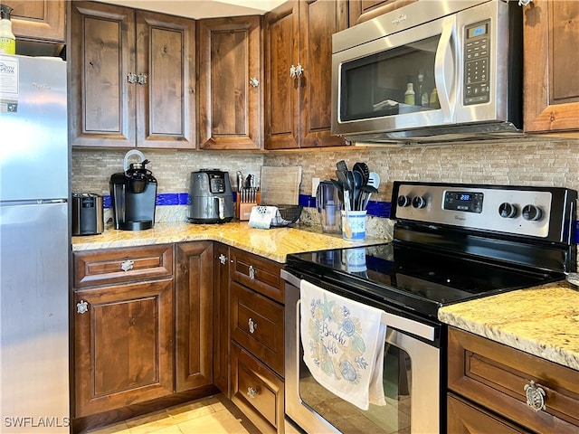 kitchen featuring stainless steel appliances, tasteful backsplash, and light stone counters