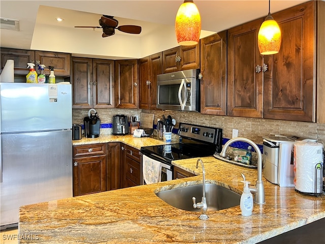 kitchen with decorative light fixtures, appliances with stainless steel finishes, sink, ceiling fan, and light stone counters