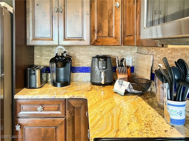 kitchen view of tasteful backsplash, stainless steel microwave, light stone countertops, and brown cabinetry