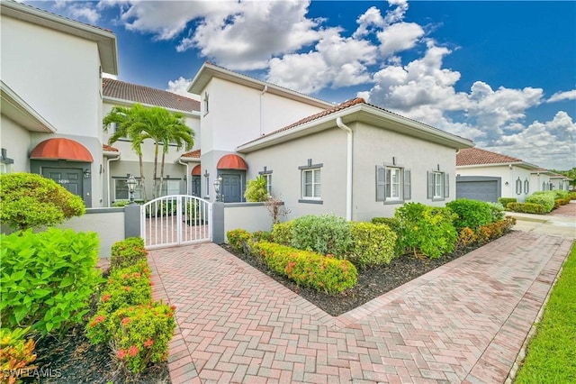 view of property exterior featuring a fenced front yard, an attached garage, a tile roof, a gate, and stucco siding