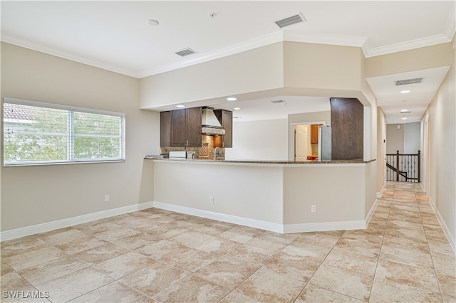 kitchen featuring wall chimney range hood, kitchen peninsula, ornamental molding, dark brown cabinetry, and stone counters