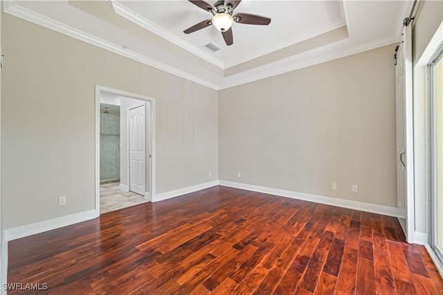 unfurnished bedroom featuring a tray ceiling, crown molding, a barn door, dark hardwood / wood-style flooring, and ceiling fan