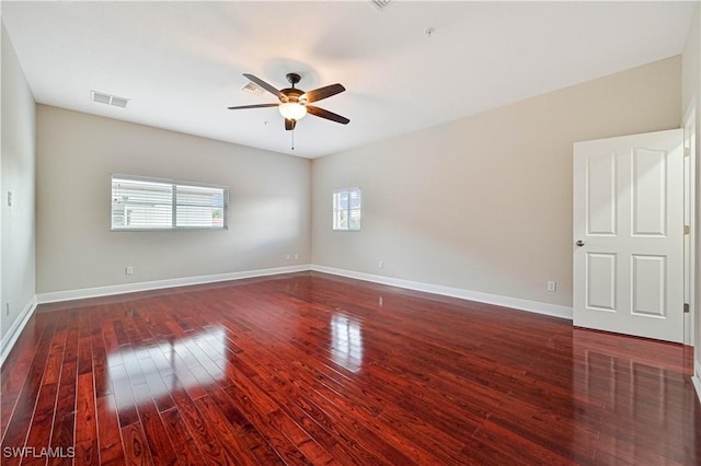 spare room with dark wood-style flooring, visible vents, ceiling fan, and baseboards