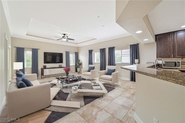 living area with plenty of natural light, a raised ceiling, and baseboards