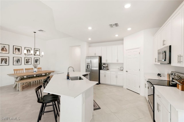 kitchen with a center island with sink, light tile patterned floors, appliances with stainless steel finishes, sink, and white cabinetry