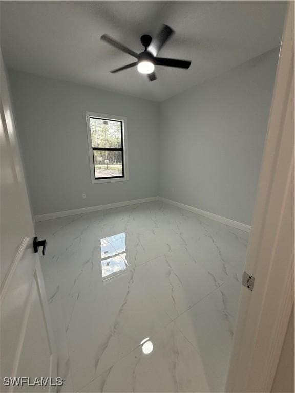 spare room featuring a ceiling fan, marble finish floor, and baseboards