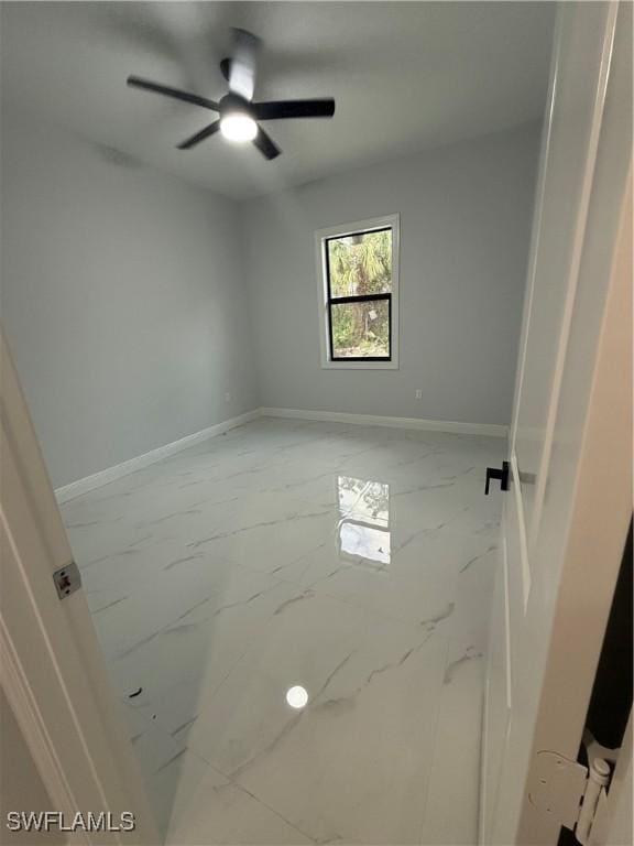 empty room with marble finish floor, a ceiling fan, and baseboards