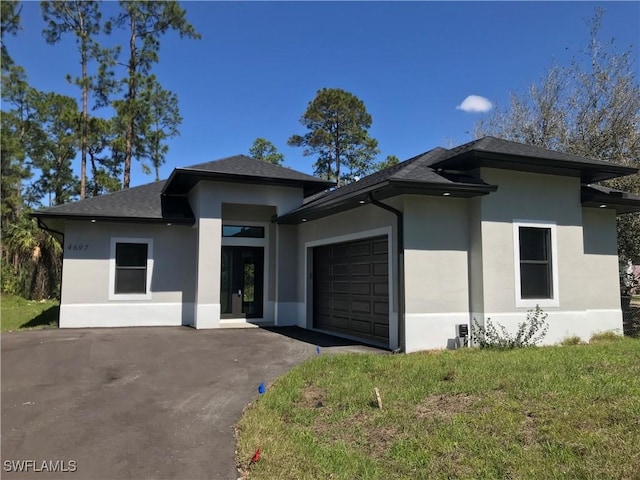 prairie-style home featuring aphalt driveway, a front lawn, an attached garage, and stucco siding