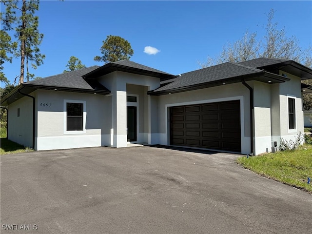 prairie-style home featuring a shingled roof, driveway, an attached garage, and stucco siding