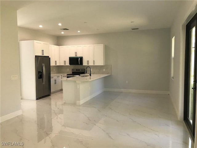 kitchen with light countertops, appliances with stainless steel finishes, white cabinets, a sink, and a peninsula