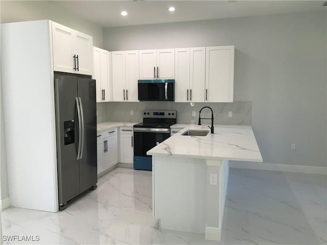 kitchen with white cabinets, appliances with stainless steel finishes, a peninsula, light stone countertops, and a sink