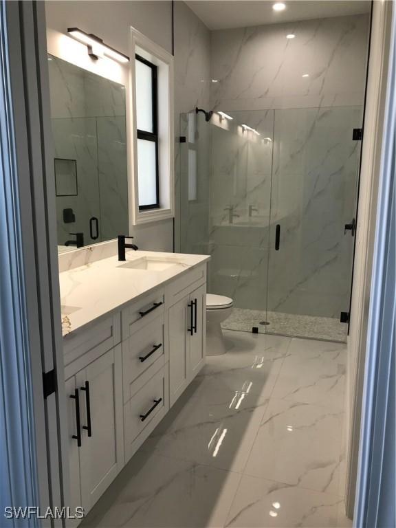 bathroom with toilet, a sink, marble finish floor, a marble finish shower, and double vanity