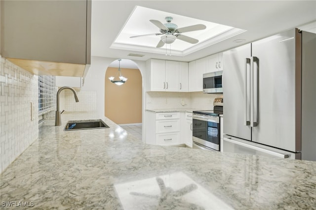 kitchen with stainless steel appliances, white cabinetry, sink, a raised ceiling, and ceiling fan