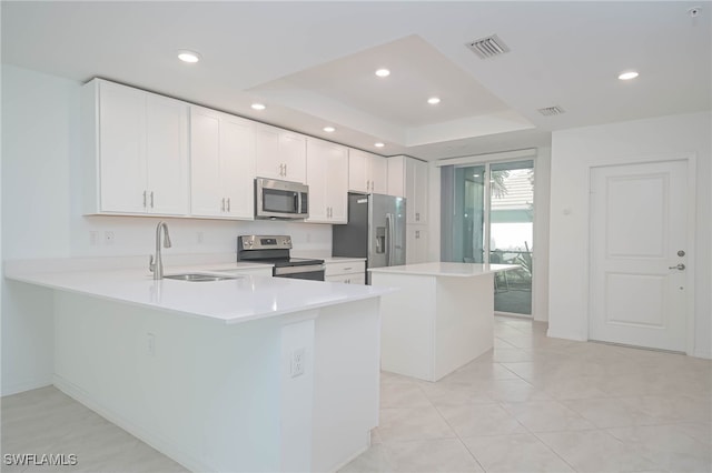 kitchen featuring light tile patterned flooring, a raised ceiling, stainless steel appliances, kitchen peninsula, and white cabinets