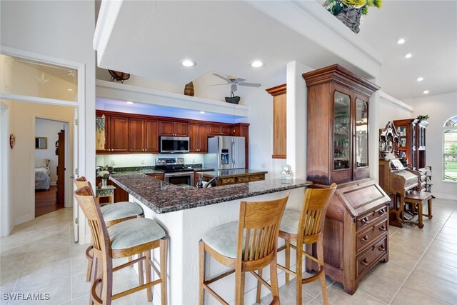 kitchen with dark stone countertops, light tile patterned floors, appliances with stainless steel finishes, a kitchen bar, and ceiling fan