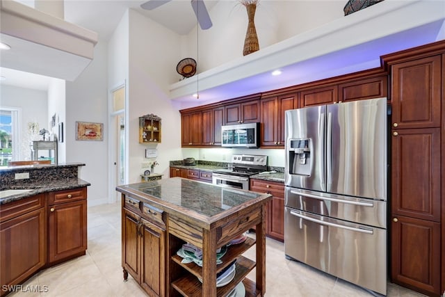 kitchen featuring ceiling fan, dark stone counters, light tile patterned floors, appliances with stainless steel finishes, and a high ceiling