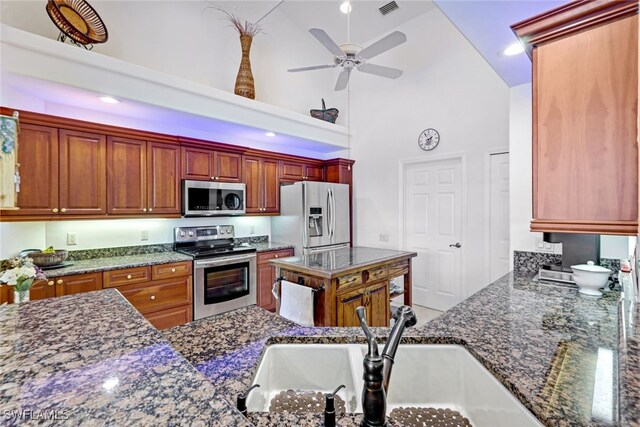 kitchen with dark stone countertops, appliances with stainless steel finishes, sink, high vaulted ceiling, and ceiling fan