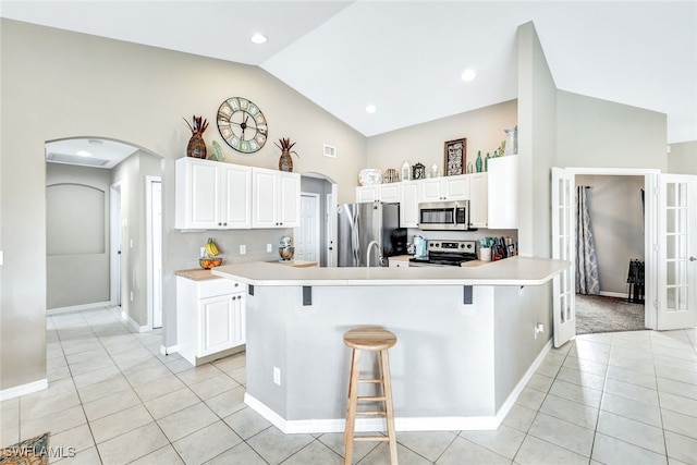 kitchen with white cabinets, stainless steel appliances, a kitchen bar, and lofted ceiling