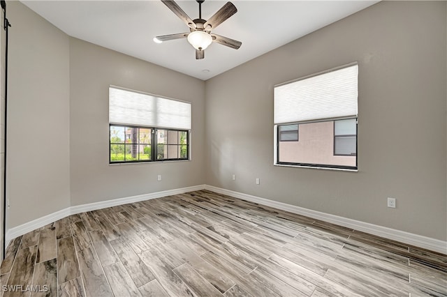 unfurnished room featuring light hardwood / wood-style flooring, a barn door, and ceiling fan