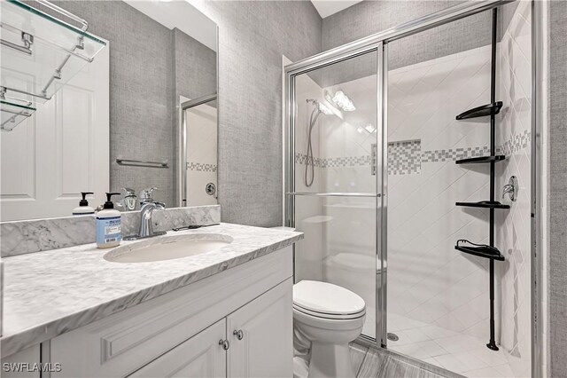 bathroom featuring a shower with door, vanity, and toilet