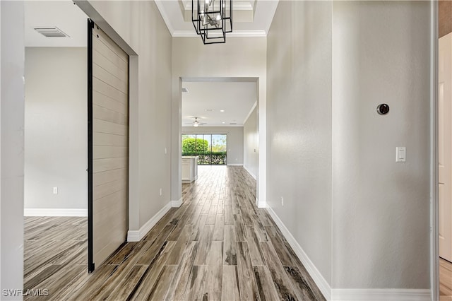 corridor featuring an inviting chandelier, crown molding, a barn door, and wood-type flooring