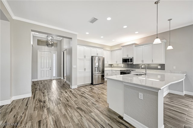 kitchen featuring a sink, stainless steel appliances, a peninsula, light wood finished floors, and decorative backsplash