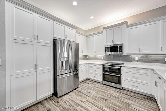 kitchen featuring crown molding, appliances with stainless steel finishes, light stone counters, and white cabinets