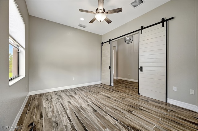 unfurnished bedroom featuring a barn door, light hardwood / wood-style flooring, and ceiling fan