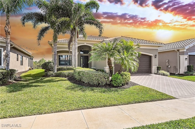 mediterranean / spanish house featuring a tile roof, a lawn, stucco siding, decorative driveway, and a garage