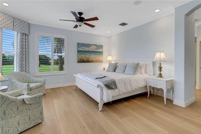 bedroom with arched walkways, visible vents, light wood-style flooring, and baseboards