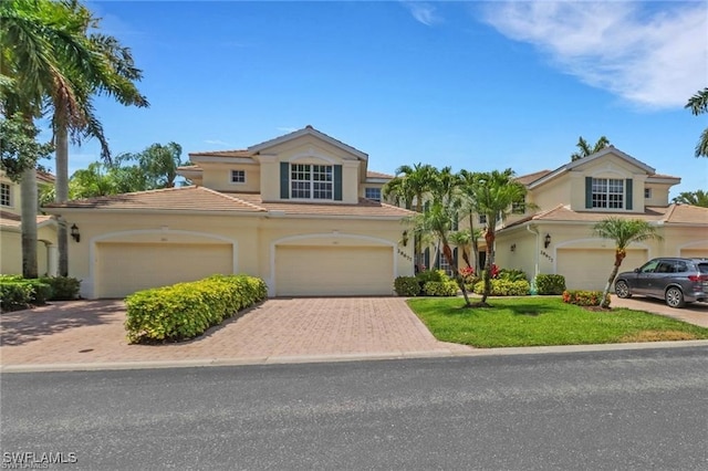 mediterranean / spanish-style home featuring decorative driveway, a tile roof, stucco siding, a front yard, and a garage