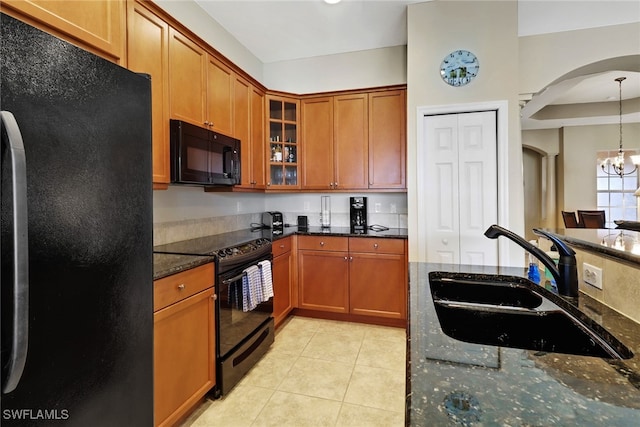 kitchen with black appliances, a notable chandelier, hanging light fixtures, sink, and dark stone counters