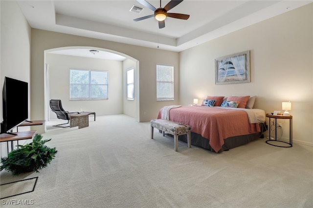 bedroom with multiple windows, a tray ceiling, light carpet, and ceiling fan