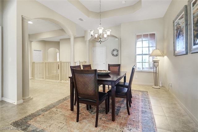 tiled dining space featuring an inviting chandelier, a tray ceiling, and ornate columns