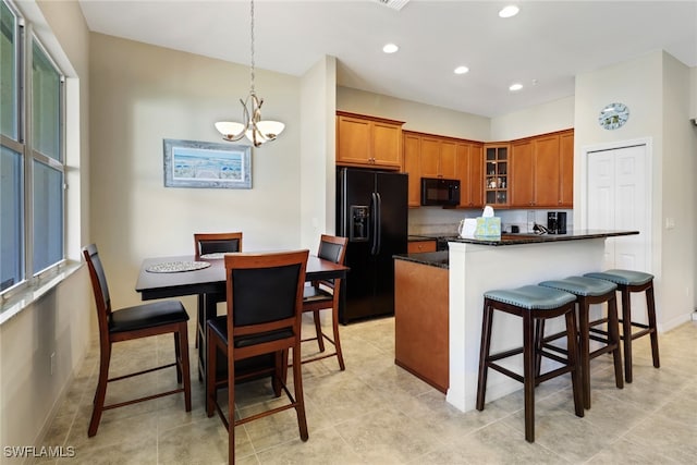 kitchen with a kitchen breakfast bar, black appliances, a chandelier, dark stone countertops, and light tile patterned flooring