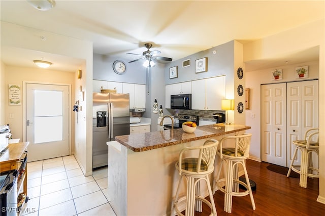 kitchen with kitchen peninsula, a kitchen breakfast bar, stainless steel appliances, white cabinets, and light hardwood / wood-style flooring