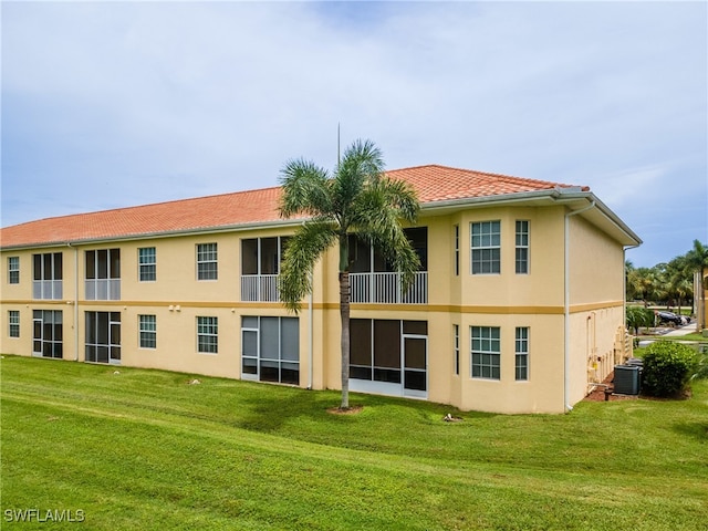 rear view of house featuring cooling unit, a lawn, and a balcony