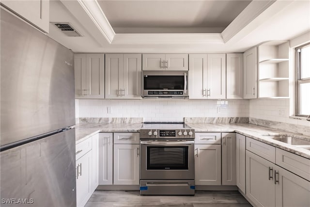 kitchen featuring a tray ceiling, appliances with stainless steel finishes, light stone countertops, and light hardwood / wood-style flooring