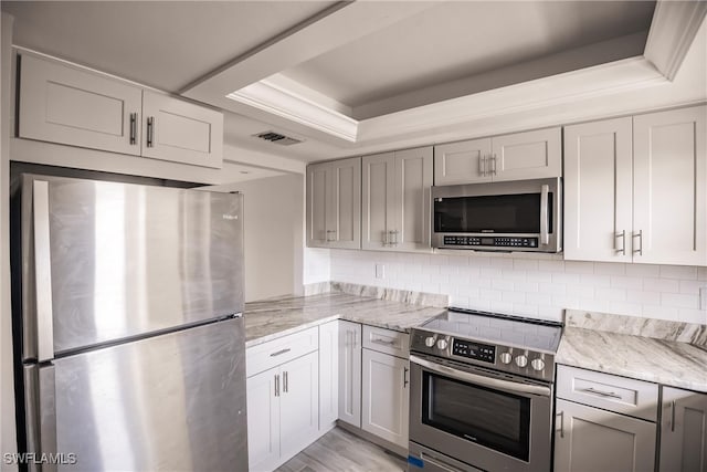 kitchen with light hardwood / wood-style flooring, stainless steel appliances, backsplash, and a tray ceiling