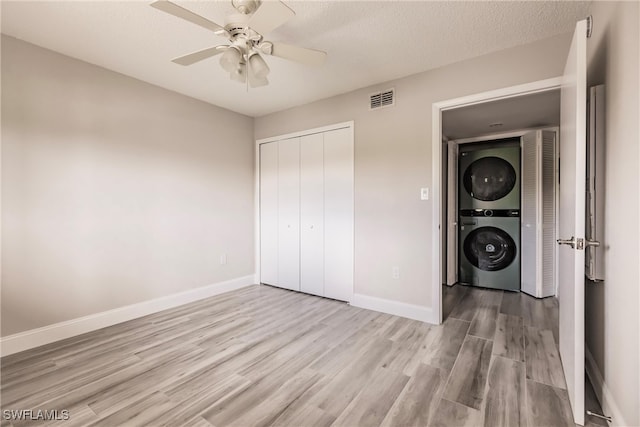 unfurnished bedroom with ceiling fan, light wood-type flooring, a closet, and stacked washer / drying machine