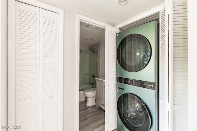 laundry room featuring wood-type flooring and stacked washer / drying machine