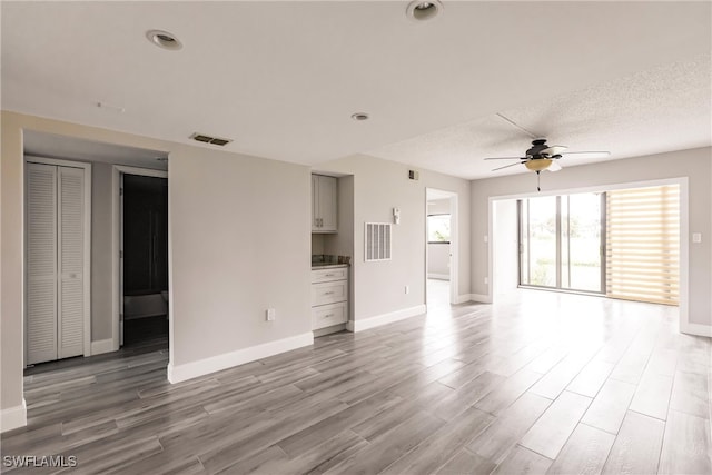 unfurnished living room featuring hardwood / wood-style floors, ceiling fan, and a textured ceiling