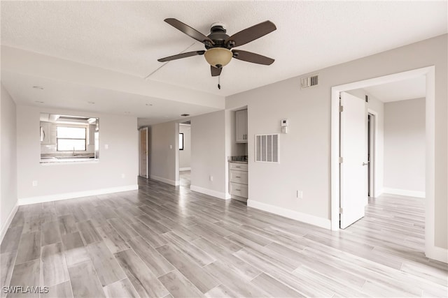 empty room featuring light wood-type flooring, ceiling fan, and a textured ceiling