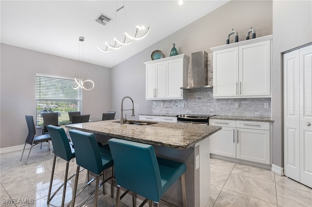 kitchen featuring wall chimney exhaust hood, white cabinets, sink, and a chandelier