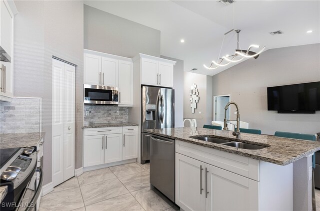 kitchen with decorative backsplash, an island with sink, vaulted ceiling, appliances with stainless steel finishes, and sink